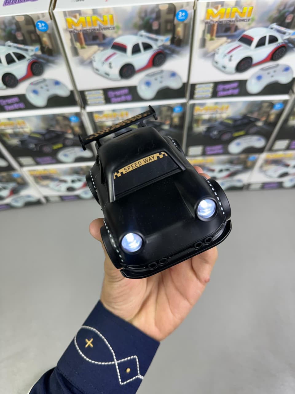 Black toy car held in a hand with a display of similar cars in the background