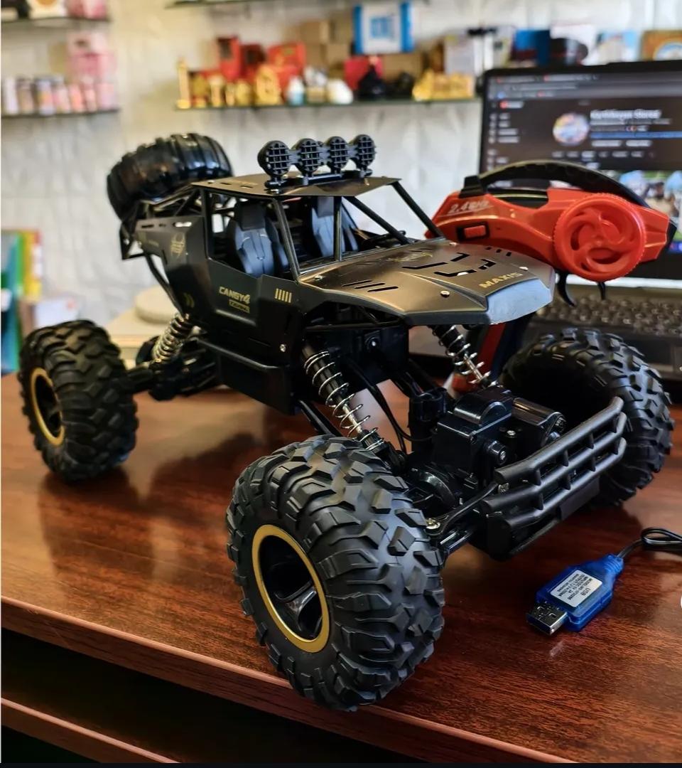 Toy monster truck with large wheels on a wooden surface, with a blurred background of a room.
