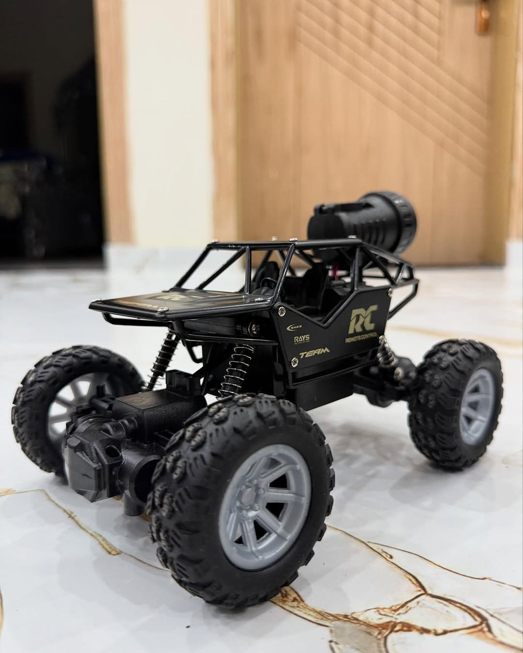 Black RC car on a marble floor with a wooden door in the background
