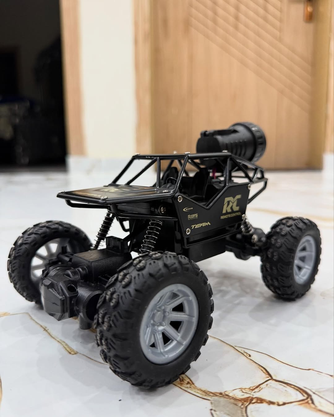 Black RC car on a marble floor with a wooden door in the background