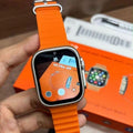 A close-up of a smartwatch with a bright orange textured strap and a silver-toned metal case, held in a hand. The watch screen is on, displaying an orange interface.